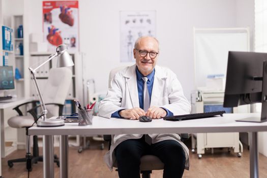 Specialist doctor wearing white coat in hospital cabinet. Medic smiling.