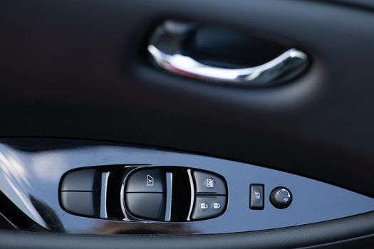 Window and mirror control panel on driver's door, detail of modern electric car. Detail on buttons controlling the windows in a car. Car interior details of door handle with windows controls