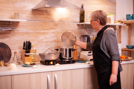 Woman preparing dinner for romantic dinner in kitchen. Retired woman cooking nutritious food for her and husband to celebrate relationship anniversary.