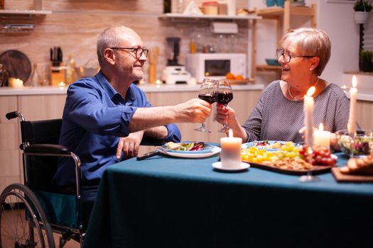 Disabled man smiling at wife while having dinner in kitchen. Wheelchair immobilized paralyzed handicapped man dining with wife at home, enjoying the meal.