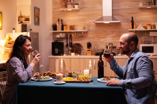 Young couple having romantic time during dinner. Happy couple talking, sitting at table in dining room, enjoying the meal, celebrating their anniversary at home having romantic time.