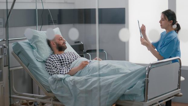 Medical woman nurse showing bones radiography examining sickness symptom. Sick man patient resting in bed discussing disease treatment in hospital ward during therapy consultation