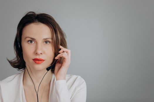 Call centre agent talking with their headset in a bright office. Call-centre lady employee happy of conversation with customer calling by headset, looking at display. Close-up of beautiful face.