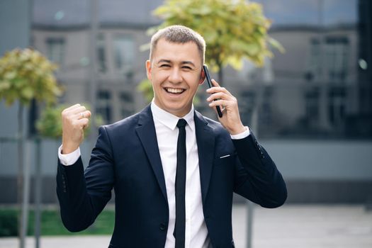 Portrait of excited man reading good news at smartphone outdoors. Successful businessman celebrating win with mobile phone outside. Surprised man looking mobile phone outside.