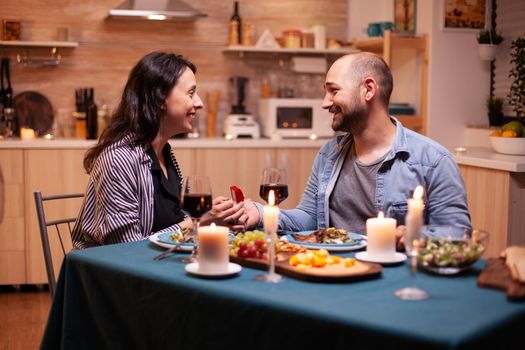 Husband proposing wife to marry him in kitchen during romantic dinner. Man making proposal to his girlfriend in the kitchen during romantic dinner. Happy caucasian woman smiling being speechless