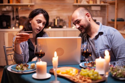Husband and wife making online payment during romantic dinner. Adults sitting at the table, searching, browsing, surfing, using technology card payment, internet.