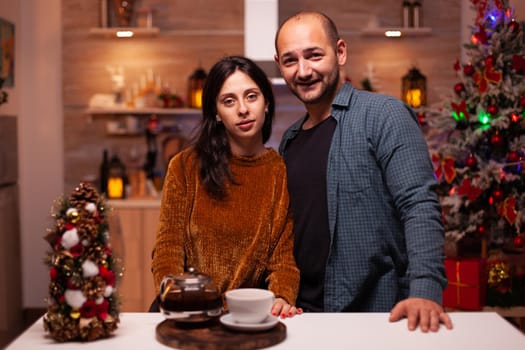 Portrait of happy family looking into camera while celebrating christmas winter holiday standing in xmas decorated kitchen. Cheerful joyful enjoying spending wintertime together. Christmastime