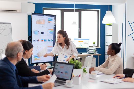 Furious company manager asking for explications from multi ethnic coleagues holding finance report in conference room. Businesswoman raging about multitasking difficult job, screaming in boardroom