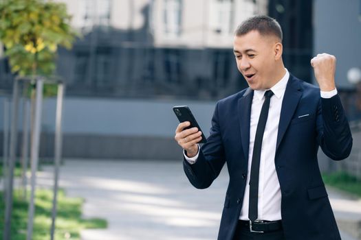 Portrait of excited man reading good news at smartphone outdoors. Successful businessman celebrating win with mobile phone outside. Surprised man looking mobile phone outside.
