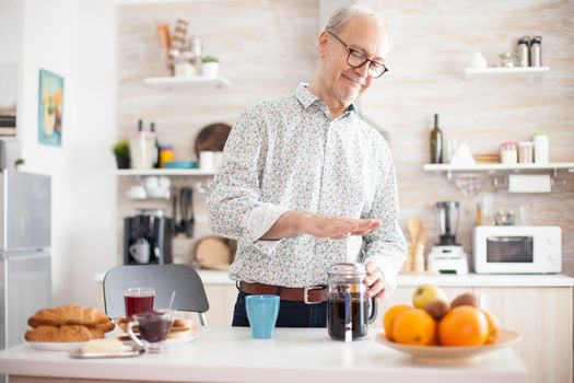 Senior man making coffee with use of a french press during breakfast in kitchen. Elderly person in the morning enjoying fresh brown cafe espresso cup caffeine from vintage mug, filter relax refreshment
