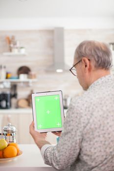 Mature man holding tablet pc with chroma key in kitchen during breakfast. Elderly person with green screen isolated mock-up mockup for easy replacement