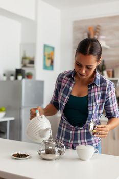Happy housewife pouring hot water in teapot to prepare the green tea for breakfast in the morning. Woman, lifestylem, beverage, preparation, herbal, teapot, morning, aromatic.