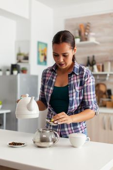 Housewife preparing hot drinkg in kitchen using aromatic herbs on teapot. Woman, lifestylem, beverage, preparation, herbal, teapot, morning, aromatic.
