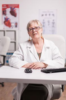 Mature female doctor in clinic cabinet looking at camera.