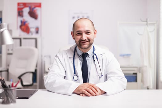 Portrait of young doctor smiling looking at the camera in hospital office wearing white coat and stethoscope.