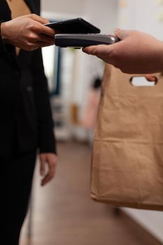 Customer paying for their order with smartphone nfc technology. Money transaction without credit card, recieving food order in paper bag. Using pos for takeaway pay.