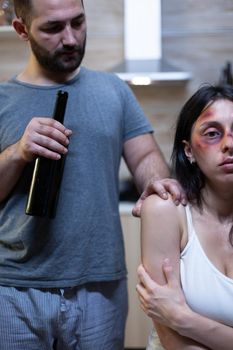 Alcoholic husband harassing abused wife with bruises. Violent man holding bottle of alcohol threatening terrified woman. Victim of domestic violence and physical trauma, marriage problem.