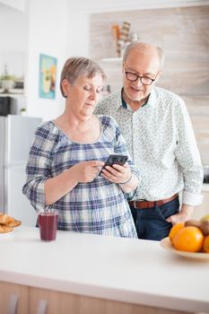 Retired couple browsing on smartphone in their cozy and bright kitchen.