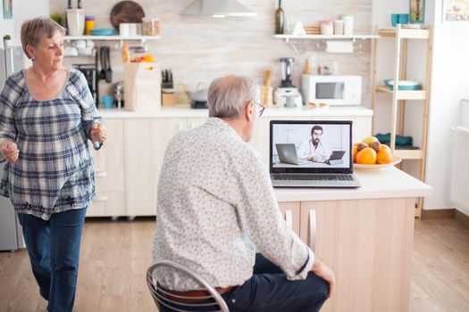 Senior couple during video conference with doctor using laptop in kitchen discussing about health problems. Online health consultation for elderly people drugs ilness advice on symptoms, physician telemedicine webcam. Medical care internet chat