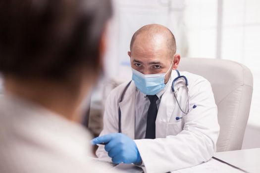 Young medic wearing protection mask against covid-19 looking at female patient during consulting.