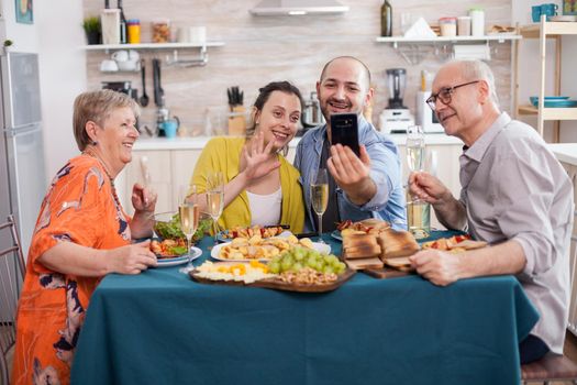 Cheerful family during video call while having delicious brunch in kitchen at dining table. Parents bonding with son and his wife.