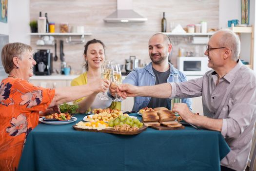 Happy family rising wine glasses during lunch. Toasting with white wine while dining in kitchen. Tasty seasoned potatoes.