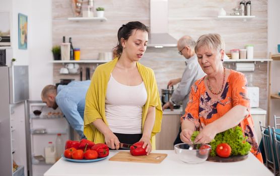 Young woman slicing bell pepper for for salad while helping her mother preparing salad during lunch.