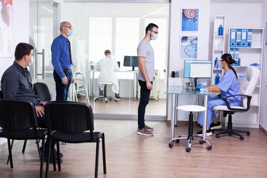 Elderly patient in hospital waiting area for coronavirus examination. Social distancing, medic, covid-19, man, worried, protection, corona, medicine, medical, nurse, talking, virus.