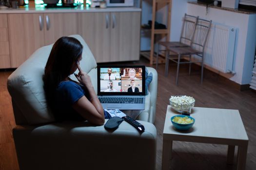 Woman speaking with colleagues on webcam lying on sofa at home. Remote worker having online meeting, video conference consulting with team using videocall working in front of laptop.