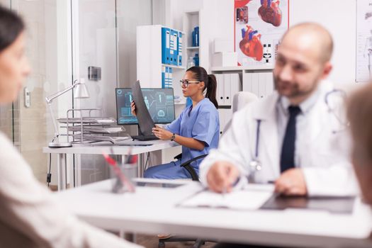 Nurse in hospital office holding x-ray image. Doctor wearing white coat during consultation of young woman and disabled mature mother in wheelchair.