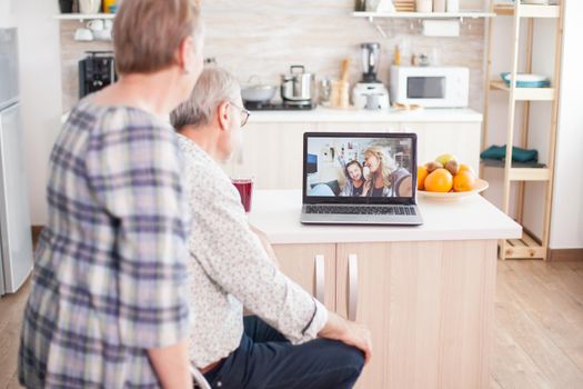 Senior couple talking with niece and daughter on online video call from kitchen. Elderly person using modern communication online internet web techonolgy.