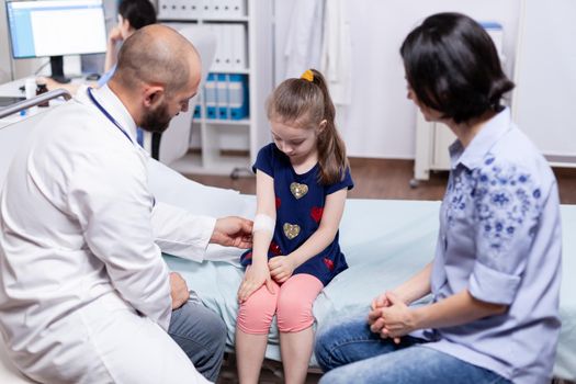 Doctor bandaging child injured hand sitting in medical office during consultation. Healthcare physician specialist in medicine providing health care services treatment examination.