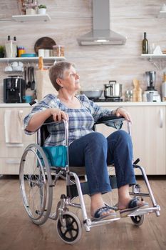 Portrait of disabled unhappy senior woman in wheelchair looking lost in kitchen. Elderly handicapped pensioner after injury and rehab, paralysis and disability for depressed invalid full of sorrow, worry and sad face. Retirement period for old people