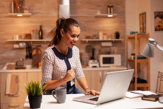 Portrait of happy businesswoman with clenched fist after finishing a deadline working from home. Employee using modern technology at midnight doing overtime for job, career, network, lifestyle.