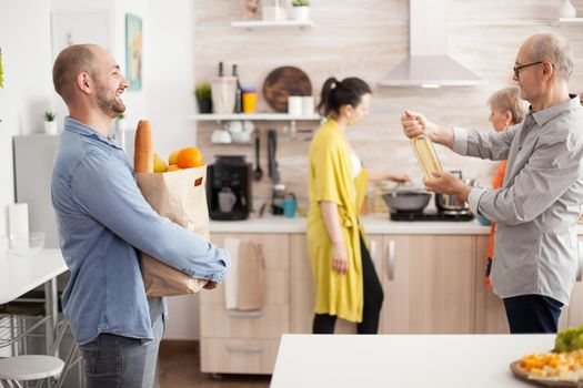 Cheerful man with groceries bag from supermarket in home kitchen. Senior man holding bottle of wine.