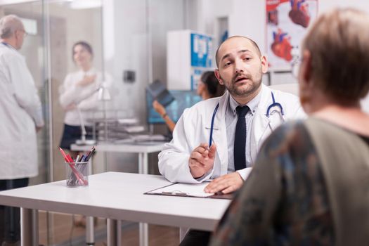 Doctor explaining illness diagnosis to senior woman during medical consultation. Mature physician discussing sickness treatment with young woman.