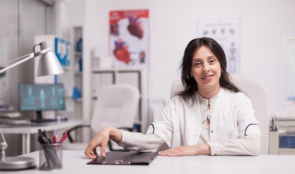 Cheerful attractive woman doctor in hospital office wearing white coat smiling to camera.