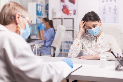 Young woman with protection mask against covid-19 crying during examination with doctor in hospital room.