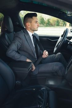 Handsome young man pinches seat belt and riding happily smiling. Joyfull driver. Lifestyle, road, car, driver concept. Protection of a person in vehicles. Road safety regulations concept