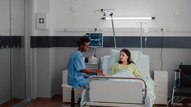 Afro-american nurse checkup sick woman analyzing pulse using medical oximeter working in hospital ward. Hospitalized patient waiting for health therapy while assistant monitoring disease recovery