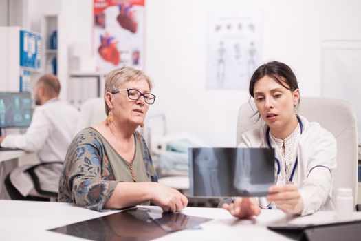 Doctor discussing with senior patient holding x-ray in hospital office. Mature woman listening doctor diagnosis.