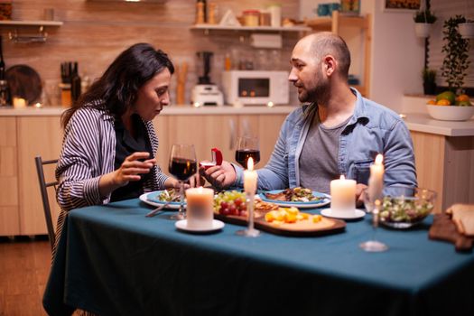 Woman surprised by marriage proposal from husband during romantic dinner. Kitchen during romantic dinner. Happy caucasian woman smiling being speechless