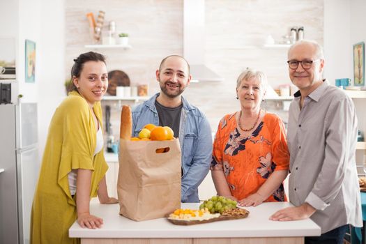 Portrait of multigenration family smiling at camera in kitchen with grocery paparbag and a variety of cheese