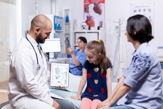 Pediatrician holding tablet pc with skeleton on tablet pc during medical examination. Healthcare physician specialist in medicine providing health care services treatment examination.