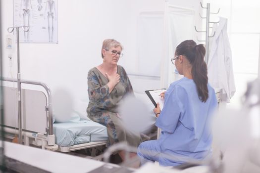 Senior patient discussing about illness with nurse during medical examination in hospital office.