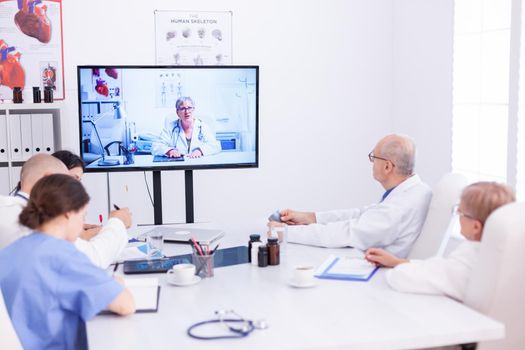 Group of doctors listening medical expert during video call in conference room. Medicine staff using internet during online meeting with expert doctor for expertise.