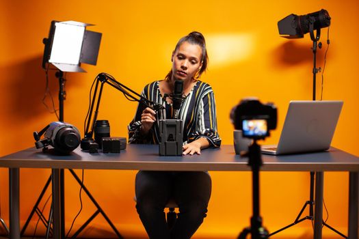 Holding microphone and talking about battery for professional videographer camera. Professional videography gear review by content creator new media star influencer on social media.