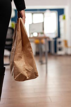 Businesswoman holding paper bag with takeaway food meal order putting on desk during takeout lunchtime in company office. Delivery man delivering fastfood packet for businesspeople.