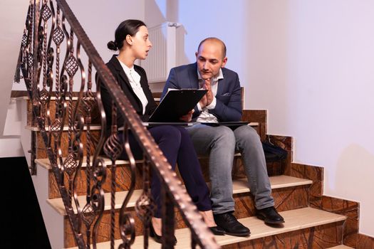 Tired stressed businessman argue with businesswoman coworker during difficult professional work deadline. Colleague entrepreneur working late together in evening at corporate job sitting on staircase, explaining difficult finance project.