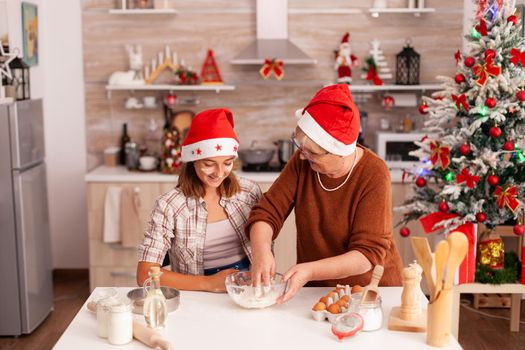 Child mixing cookies ingredients in bowl making traditional homemade dough with grandmother celebrating christmas holiday together in xmas decorated kitchen. Kid enjoying winter season baking dessert